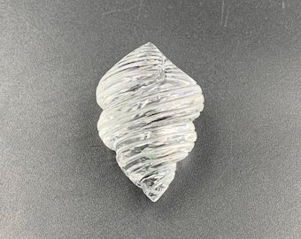 Puede incluir: Adorno de concha de cristal transparente en forma de espiral. El adorno tiene una superficie texturizada con una serie de surcos horizontales. La concha es un artículo decorativo, para la decoración del hogar.