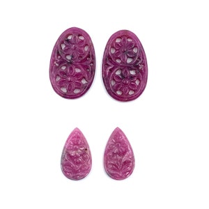 May include: Four pink carved gemstone beads. Two are oval shaped with a floral design and two are teardrop shaped with a floral design.