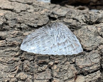Puede incluir: Un plato de vidrio transparente en forma de corazón con una superficie texturizada. El plato está sobre un trozo de corteza de árbol.