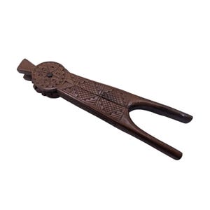 Può includere: Un schiaccianoci in legno con intagli intricati. Lo schiaccianoci è marrone e ha un design unico con un'apertura circolare al centro.