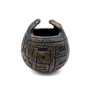 Könnte beinhalten: Ein kleiner, runder Keramiktopf mit einem geometrischen Muster in Grün und Braun. Der Topf hat zwei kleine, abgerundete Griffe oben.