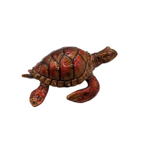May include: A small, red and brown ceramic turtle figurine with a detailed shell and rhinestones. The turtle is in a swimming position with its head and legs extended.