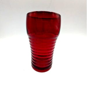 Könnte beinhalten: Ein rubinroter Glasbecher mit abgerundeter Oberseite und geripptem, zylindrischem Boden. Das Glas ist transparent. Der Becher wird wahrscheinlich für Getränke verwendet. Vintage-Design.
