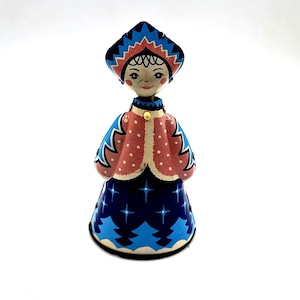 May include: A vintage Russian nesting doll, featuring a stylized woman in a traditional outfit. The doll has a blue and red patterned hat and dress, with a pink jacket adorned with white polka dots. The doll is approximately 6 inches tall.