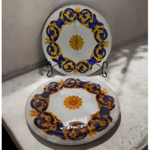 May include: Two white ceramic plates with a blue and gold floral design. The plates have a white center with a gold and yellow floral design.