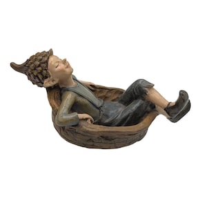 Könnte beinhalten: Eine skurrile Figur eines kleinen Elfen, der sich in einer hölzernen Wiege ausruht. Der Elf trägt ein grünes Hemd und dunkle Hosen, mit spitzen Ohren und einem gelassenen Gesichtsausdruck. Die Wiege hat eine natürliche braune Farbe.