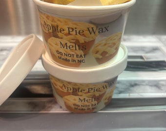 May include: A white container with a lid filled with apple pie wax melts. The container has a label that reads "Apple Pie Wax Melts, Do Not Eat, Made in NC".