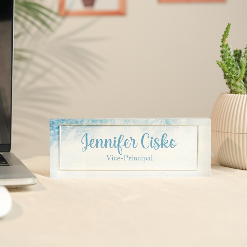 May include: A rectangular desk nameplate with the name "Jennifer Cisko" and the title "Vice-Principal" in light blue script. The nameplate has a blue and white watercolor-style border and sits on a light-colored desk.