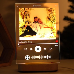 Könnte beinhalten: Eine klare Acryllampe mit einem Holzsockel. Die Lampe zeigt ein Foto eines Paares, eine Musikplayer-Oberfläche und den Text "Dein Lieblingslied".