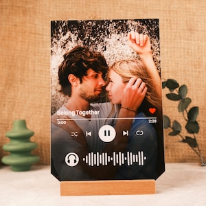 Könnte beinhalten: Ein schwarzer Acryl-Bilderrahmen mit einem Foto eines Paares und einer Musikplayer-Oberfläche. Die Oberfläche zeigt den Songtitel "Belong Together", die Zeit 0:00, einen Play-Button und die Zeit 2:28. Der Rahmen steht auf einem Holzständer.