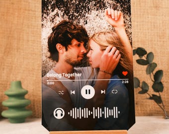 Op de afbeelding: Een zwart acryl fotolijstje met een foto van een stel en een muziekspelerinterface. De interface toont de titel van het nummer "Belong Together", de tijd 0:00, een afspeelknop en de tijd 2:28. Het lijstje staat op een houten standaard.