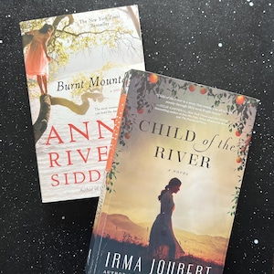 May include: A white ceramic mug with a black handle and the text "But First, Coffee" in a bold, black font. The mug is set against a blurred background, suggesting a cozy setting.