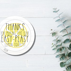 Może przedstawiać: Okrągła biała naklejka z żółtym cytrynowym wzorem i tekstem "THANKS FOR MAKING THIS YEAR EASY-PEASY LEMON-SQUEEZY! FROM"