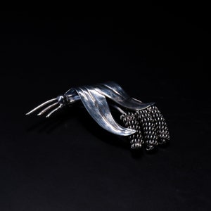 Peut inclure: Une broche en argent en forme de fleur avec un groupe de petites perles. La broche est en métal et a une surface texturée.