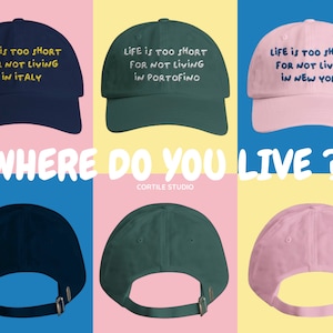 Può includere: Un assortimento di cappellini da baseball blu navy, verdi e rosa, ognuno ricamato con la frase "LIFE IS TOO SHORT FOR NOT LIVING" seguita da una località: Italia, Portofino e New York. L'immagine include anche il testo "WHERE DO YOU LIVE?" e "CORTILE STUDIO".