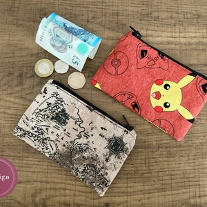 Può includere: Due piccole pochette con cerniera. Una pochette è rossa con un personaggio Pikachu giallo e un design Pokeball. L'altra pochette è marrone con un design di mappa.
