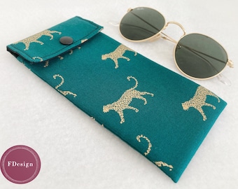 Pode incluir: Um estojo para óculos de sol de tecido azul turquesa com fecho de aba e botão dourado. O estojo é decorado com um padrão repetido de silhuetas de leopardos dourados.