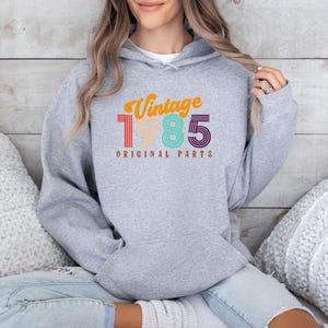 May include: Gray hooded sweatshirt with the text "Vintage 1985 Original Parts" in rainbow colors.
