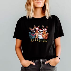 May include: Black t-shirt with a festive graphic of five chickens. Each chicken is adorned with Santa hats, reindeer antlers, and scarves. The chickens are in shades of blue, brown, and white, perfect for the holiday season.