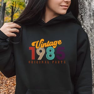 May include: Black hoodie with a vintage 1985 design in rainbow colors. The text "Vintage 1985 Original Parts" is printed on the hoodie.