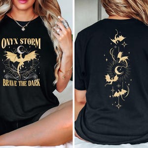 May include: Black t-shirt with a gold graphic of a dragon and the text "ONYX STORM" and "BRAVE THE DARK". The back of the shirt has a gold graphic of a crescent moon and several bats.