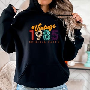May include: Black hooded sweatshirt with a vintage 1985 design in rainbow colors. The text "Vintage 1985 Original Parts" is printed on the front.