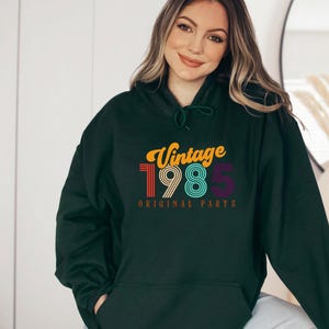 May include: A dark green hooded sweatshirt with the text "Vintage 1985 Original Parts" in colorful retro font.