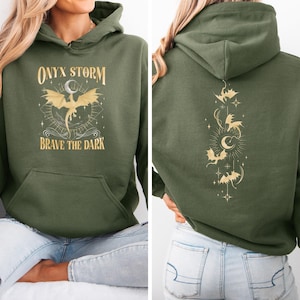 May include: A green hooded sweatshirt with the text "ONYX STORM" and a gold dragon design on the front. The back of the sweatshirt has a gold dragon design with the text "BRAVE THE DARK".