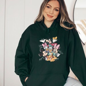 May include: Dark green hoodie featuring a colorful graphic of Disney characters including Mickey Mouse, Minnie Mouse, Donald Duck, Daisy Duck, Goofy, and Pluto. The graphic has a vintage style with character signatures.