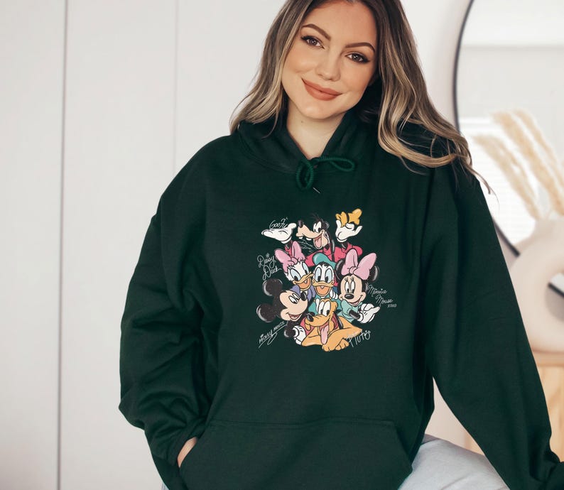 May include: Dark green hoodie featuring a colorful graphic of Disney characters including Mickey Mouse, Minnie Mouse, Donald Duck, Daisy Duck, Goofy, and Pluto. The graphic has a vintage style with character signatures.