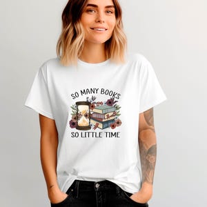 May include: White t-shirt with a graphic featuring an hourglass, books, and floral accents. The text reads "SO MANY BOOKS SO LITTLE TIME". The design includes a stack of books in shades of blue, green, and brown.