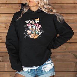 May include: Black hooded sweatshirt featuring a colorful graphic of Disney characters including Mickey Mouse, Minnie Mouse, Donald Duck, Daisy Duck, Goofy, and Pluto. The graphic includes character signatures. The sweatshirt has a front pocket.