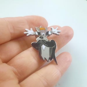 Peut inclure: Une broche en émail métallique représentant un personnage de dessin animé avec un visage gris, une grande moustache noire et des gants blancs. Le personnage a une petite touffe de cheveux orange sur la tête et les bras écartés.