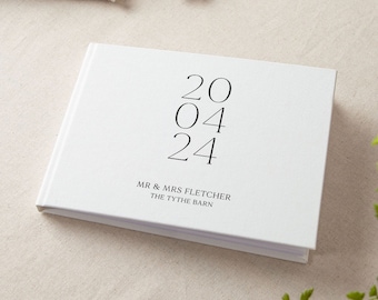 以下が含まれることがあります： 日付が黒で「20 04 24」と印刷され、その下に「MR & MRS FLETCHER THE TYTHE BARN」というテキストが印刷された白いゲストブックです。