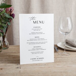 May include: A white wedding menu with a simple script font. The menu lists starters, mains, and desserts. The bottom of the menu includes the names Laurie & Daniel and the date 27th September 2024.