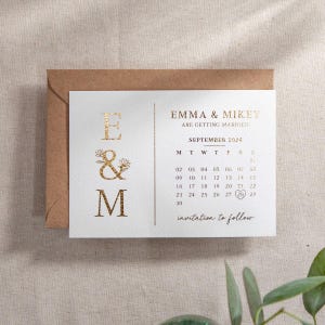 May include: Gold foil save the date card with a calendar showing September 2024 with the 26th circled. The card has the names Emma & Mikey and the text "Are getting married".