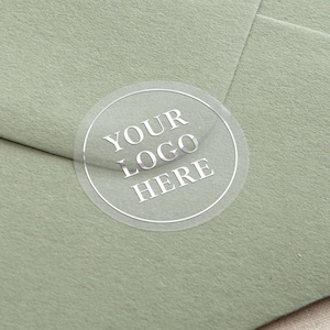 May include: A clear round sticker with the text "YOUR LOGO HERE" in silver lettering on a sage green envelope.