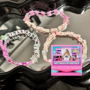 May include: Three beaded bracelets with white letter beads spelling out "GIRLS GONE WILD", "PINK PUSH UP BRA", and "MUTUAL MASTURBATION". A small pink computer graphic with the text "HOT SINGLES IN YOUR AREA" is also present.