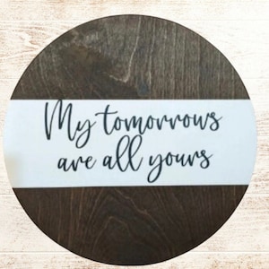 May include: A round wooden sign with a white stripe across the middle. The sign says "My tomorrows are all yours" in black cursive lettering.