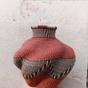 May include: A large, woven basket with a rounded, irregular shape. The basket is made of natural fibers and has a brown and black striped pattern. The basket is sitting on a stone surface.