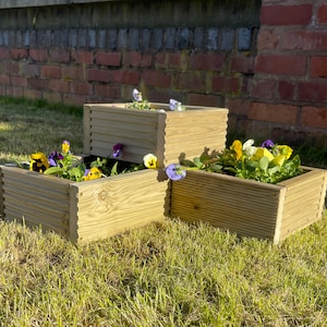 May include: A set of four wooden planter boxes stacked in a pyramid shape. The boxes are made of natural wood and have a rustic look. The boxes are filled with colourful flowers, including purple, yellow, and white.