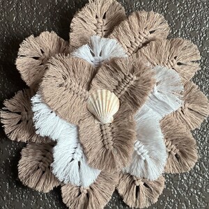 May include: A beige and white macrame flower with a small white seashell in the center.