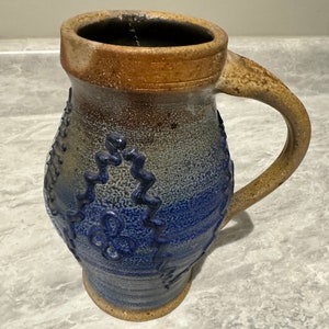 May include: A blue and brown ceramic mug with a handle. The mug has a textured surface and a design of blue flowers and leaves.