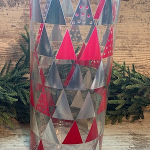 May include: A clear glass cylinder vase with a geometric pattern of red and silver triangles. The vase is decorated with a repeating pattern of triangles.