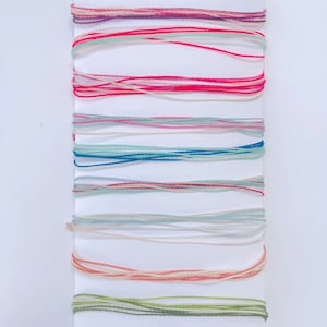 May include: A collection of embroidery floss spools in various colors, including pink, red, blue, green, and white. The spools are arranged in rows on a white background.