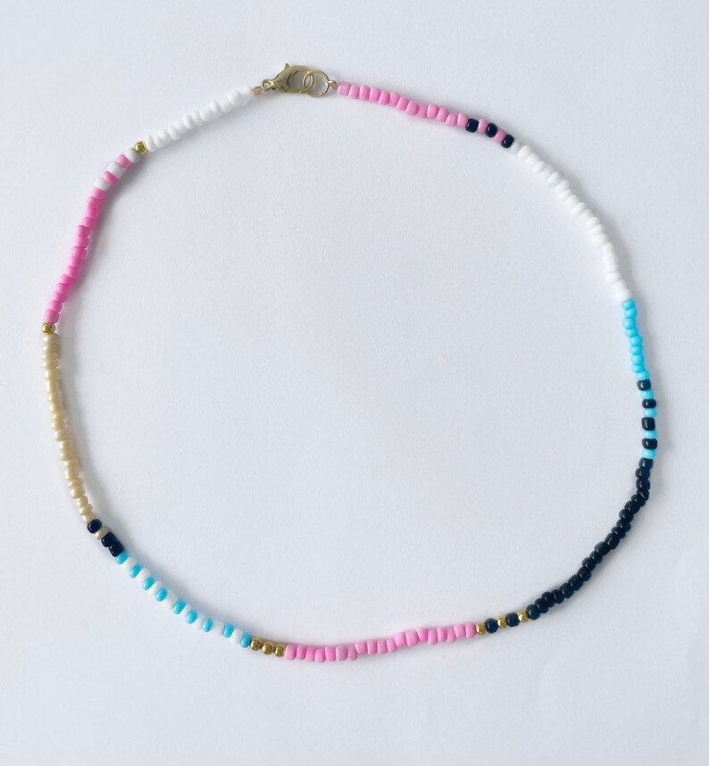 May include: A multi-colored beaded necklace with pink, white, blue, black, and gold beads.