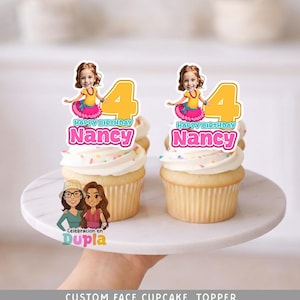 May include: Two cupcakes with white frosting and sprinkles, each topped with a custom face topper. The toppers feature a girl, the number 4, and the name "Nancy" with "Happy Birthday" text. The cupcakes sit on a white marble cake stand.