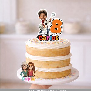 May include: A layered cake with white frosting and colorful sprinkles, topped with a custom cake topper. The topper features a cartoon image of a boy playing a guitar, the number 8, and the name "Carlos". The words "Happy Birthday" are also visible.