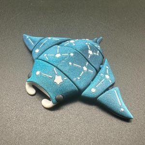 Könnte beinhalten: Türkisfarbene Mantarochen-Figur mit weißem Sternbildmuster. Die Figur hat eine strukturierte Oberfläche und weiße Akzente auf der Unterseite. Der Mantarochen ist ein Meerestier und ein dekorativer Gegenstand.