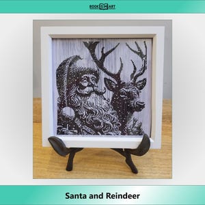 Può includere: Un'immagine incorniciata in bianco di un'illustrazione in bianco e nero di Babbo Natale e una renna. L'immagine è su un cavalletto di legno.